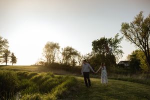 Two people walk together through a scenic countryside landscape at sunset.