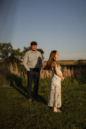 A couple poses in a grassy field during sunset wearing casual attire.