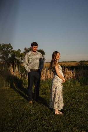 Two people stand apart in a meadow during golden hour.