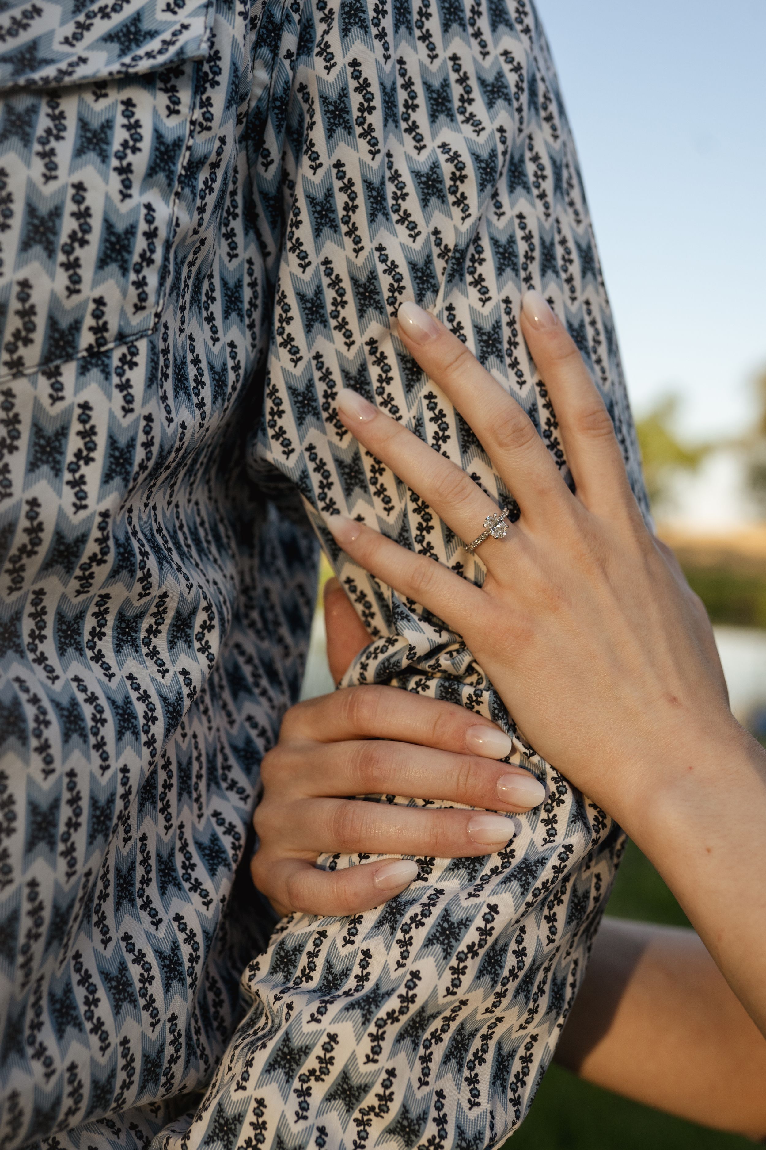 Hands gently press against a patterned fabric showing an engagement ring.