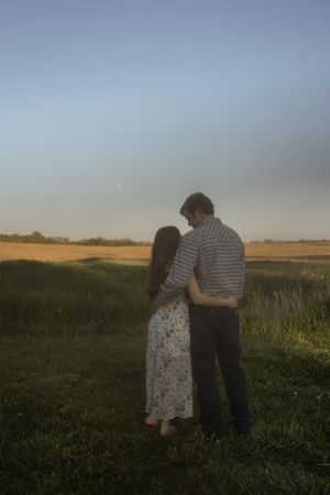 A romantic moment captured between two people in a dusky field.