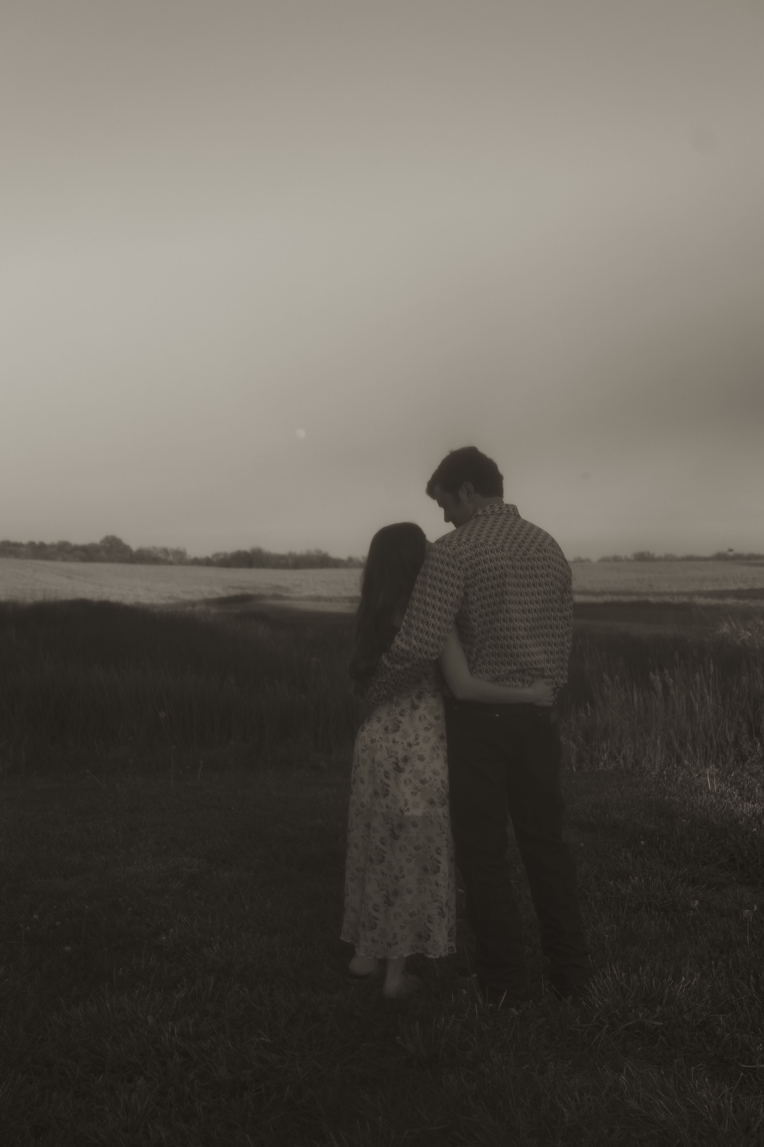 Romantic silhouette of couple standing in a rural field at dusk.