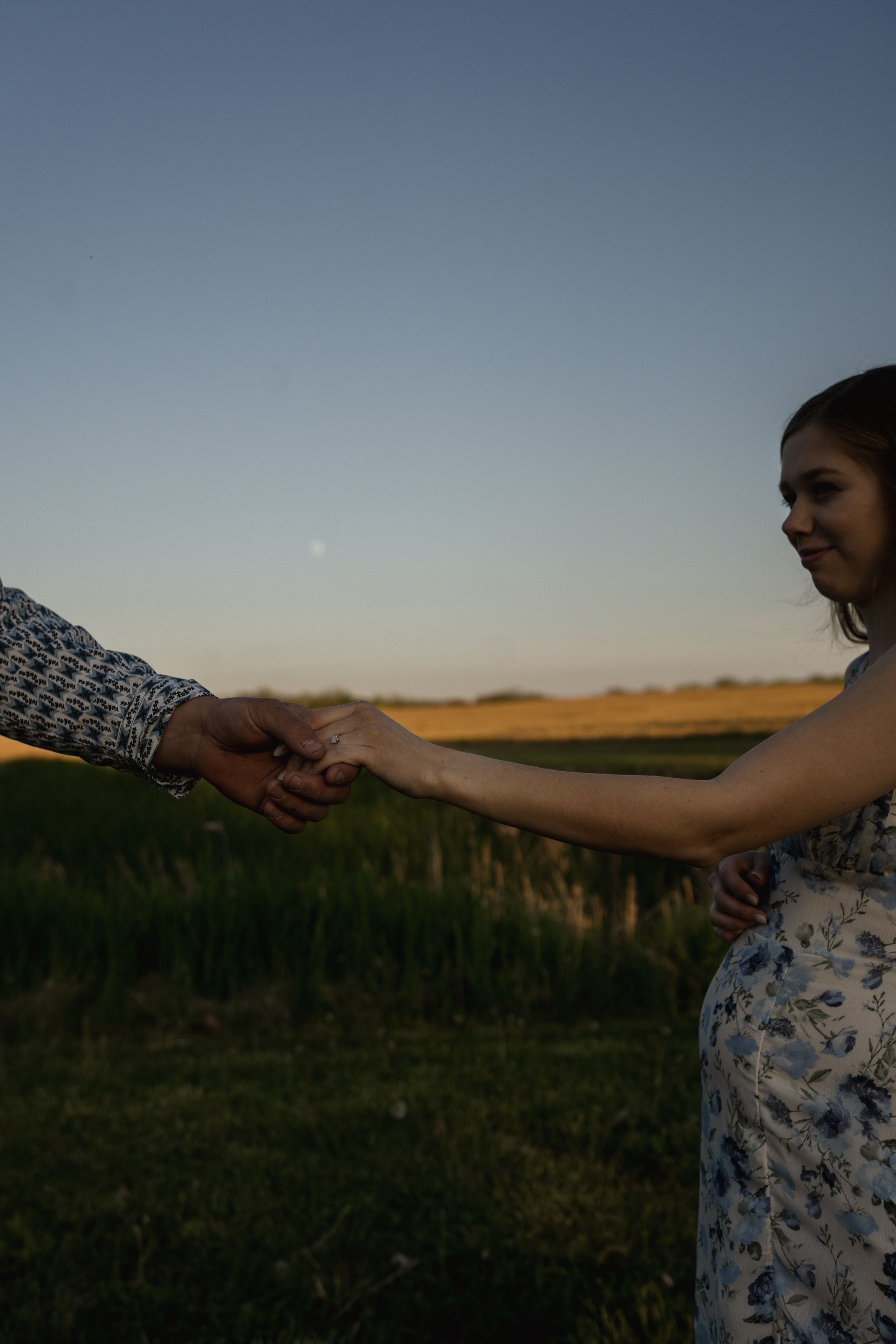Couple holds hands tenderly in a sunlit field during golden hour.