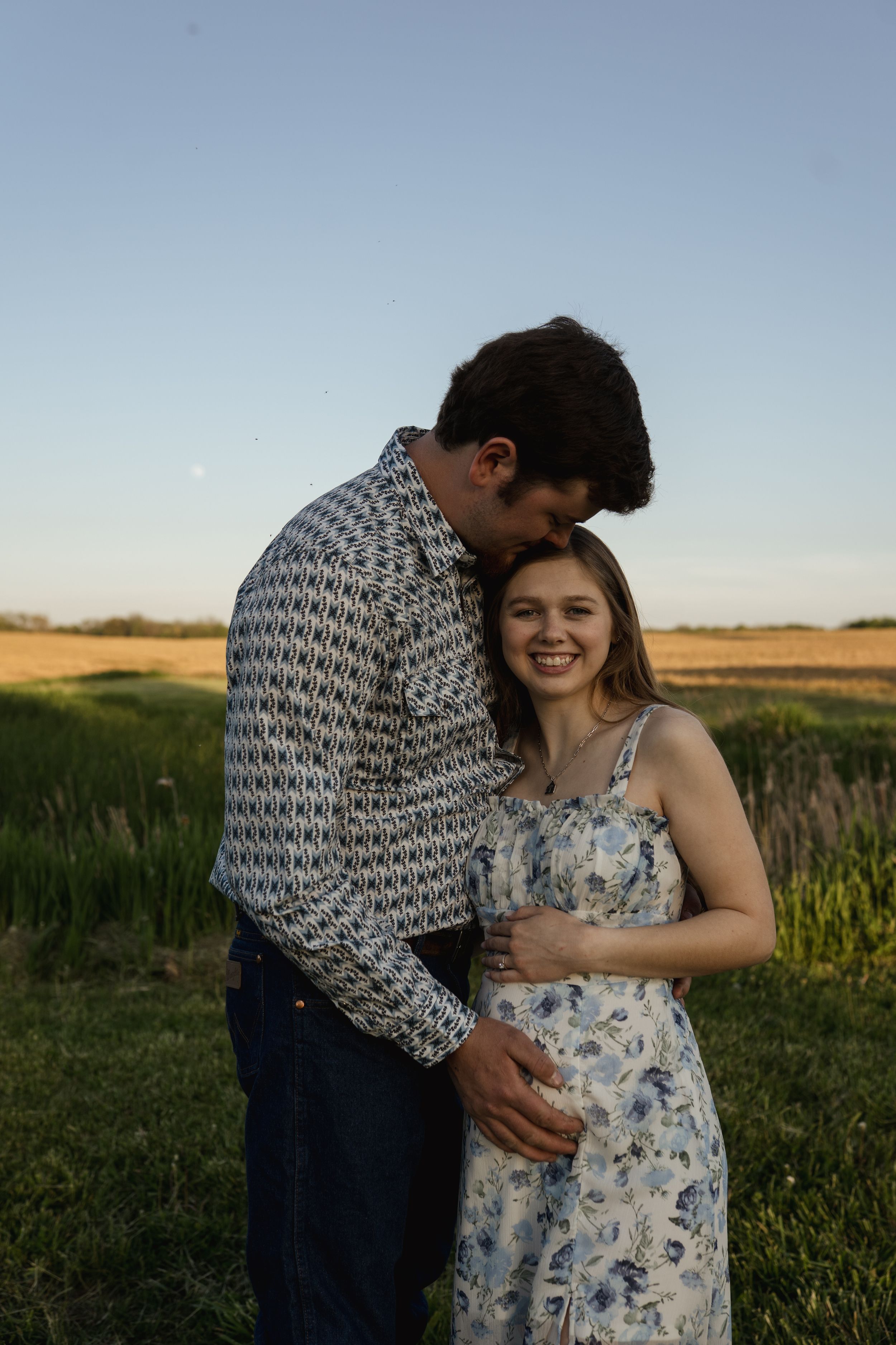 Romantic couple shares intimate moment in field during sunset.