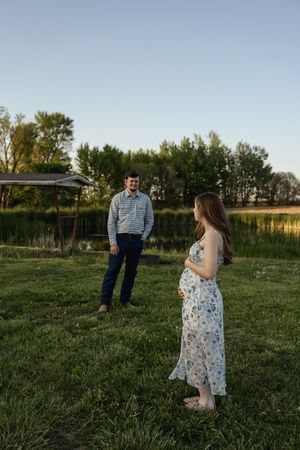 Two people share a moment together in an open field with trees lining the horizon.
