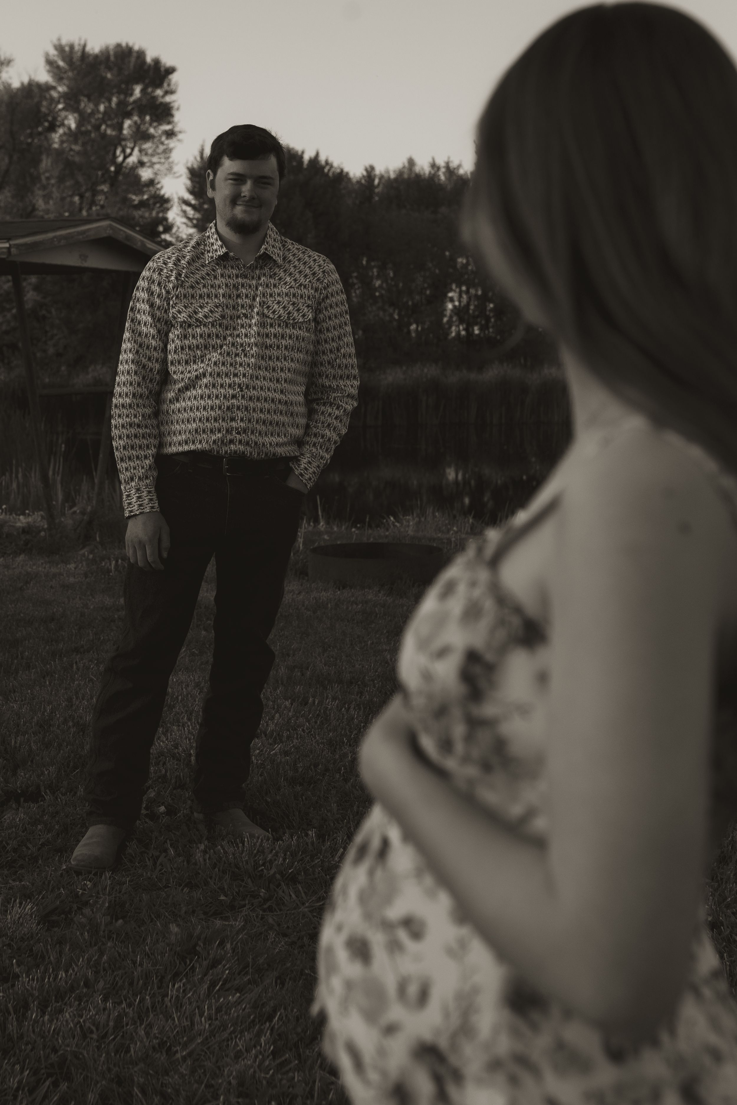 A romantic black and white portrait of two people in a field at dusk.
