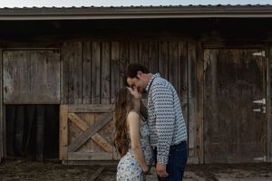 Romantic couple embraces in front of rustic barn at sunset.