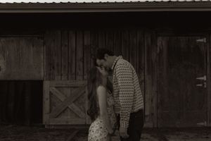 Silhouetted figures share intimate moment against weathered barn wall.