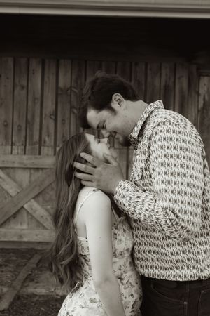 Tender moment captured between couple in black and white against barn backdrop.