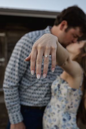 An artistic engagement ring shot with a couple embracing in soft focus background.