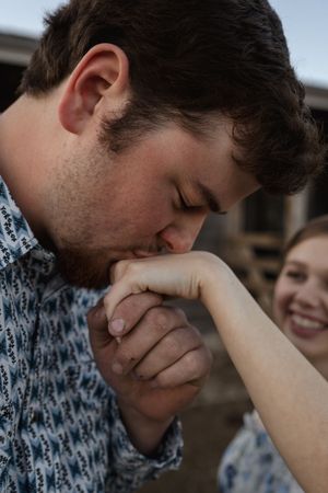 A tender moment captured as someone kisses a hand against an outdoor backdrop.