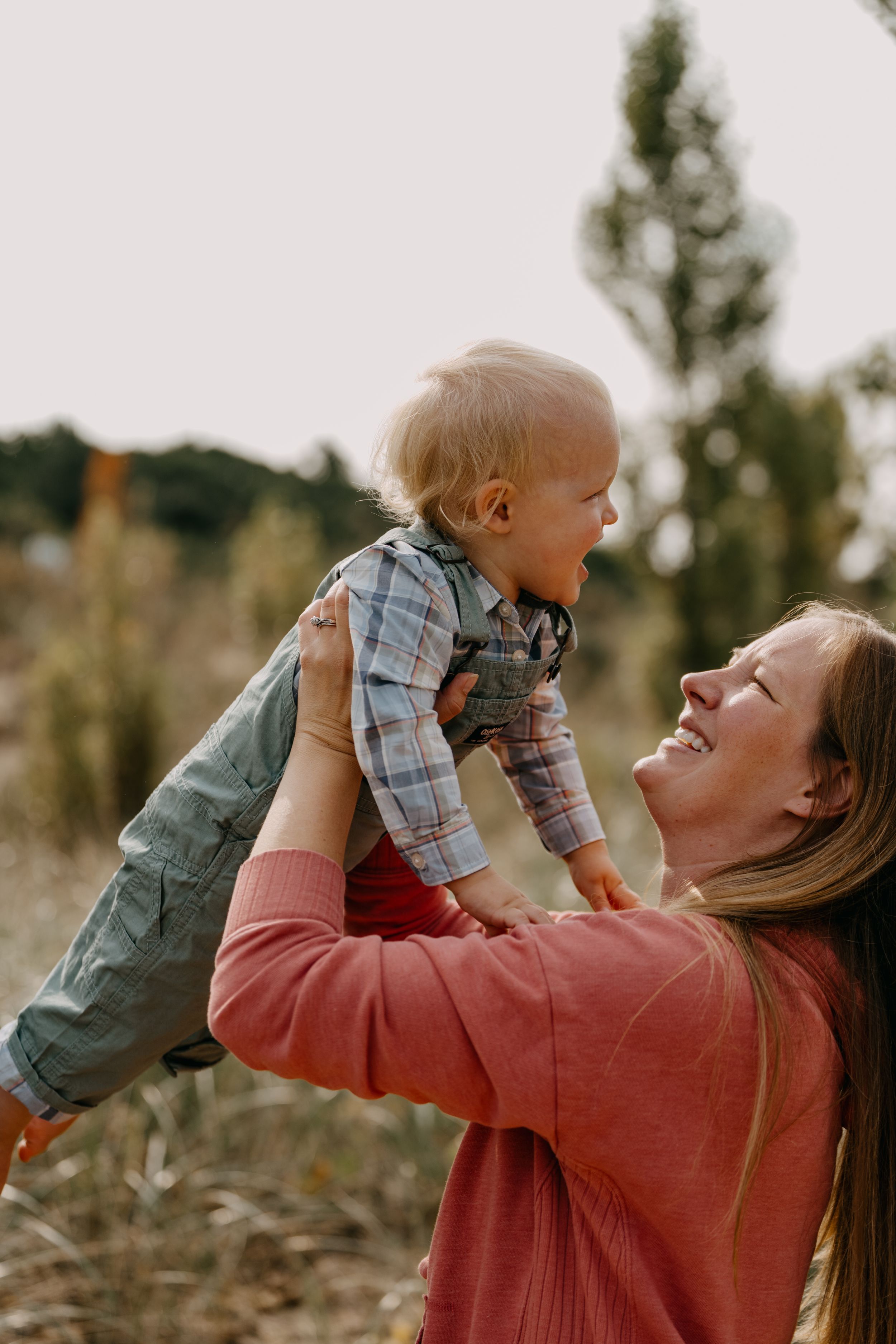 Candid outdoor moment of parental bonding and joy as a small child is lifted up high in autumn surroundings.