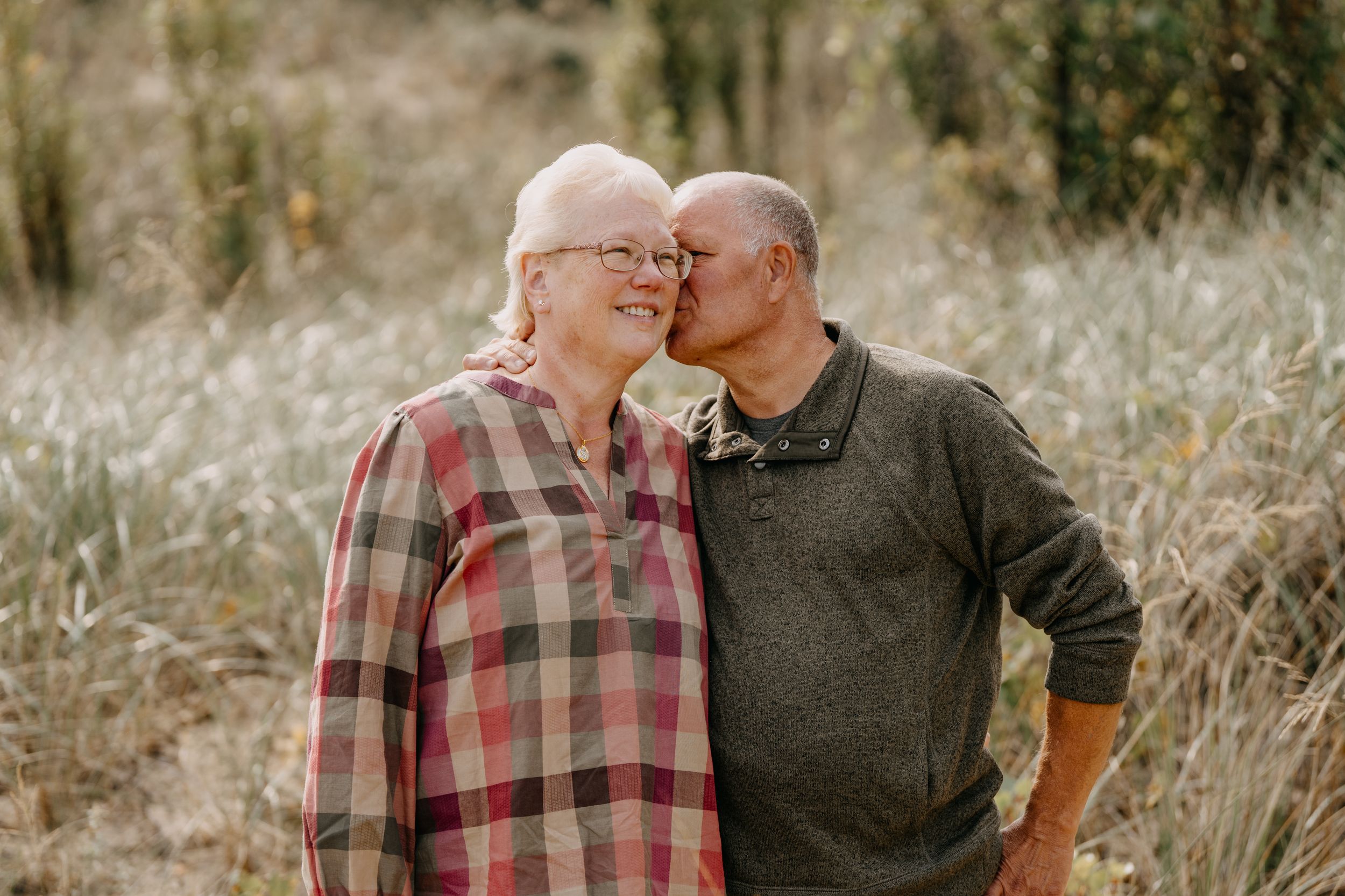 Two people share an intimate and tender moment while standing in a grassy field on a sunny autumn day.