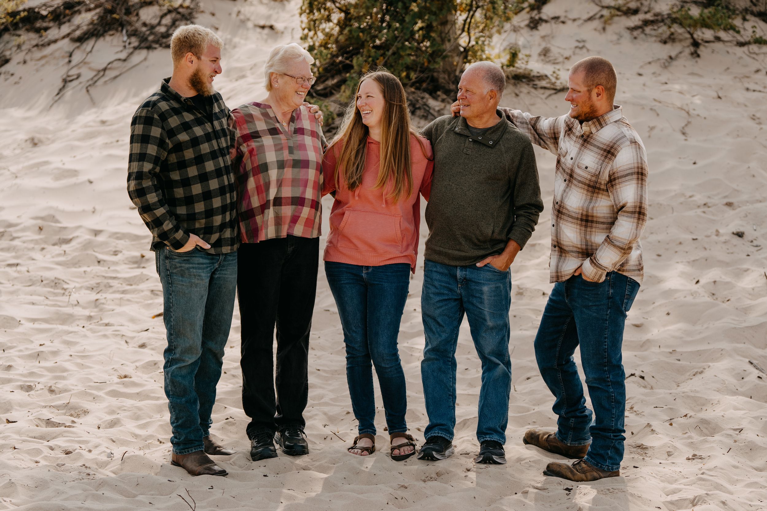 Five people in casual plaid shirts and jeans standing together on a sandy beach path.