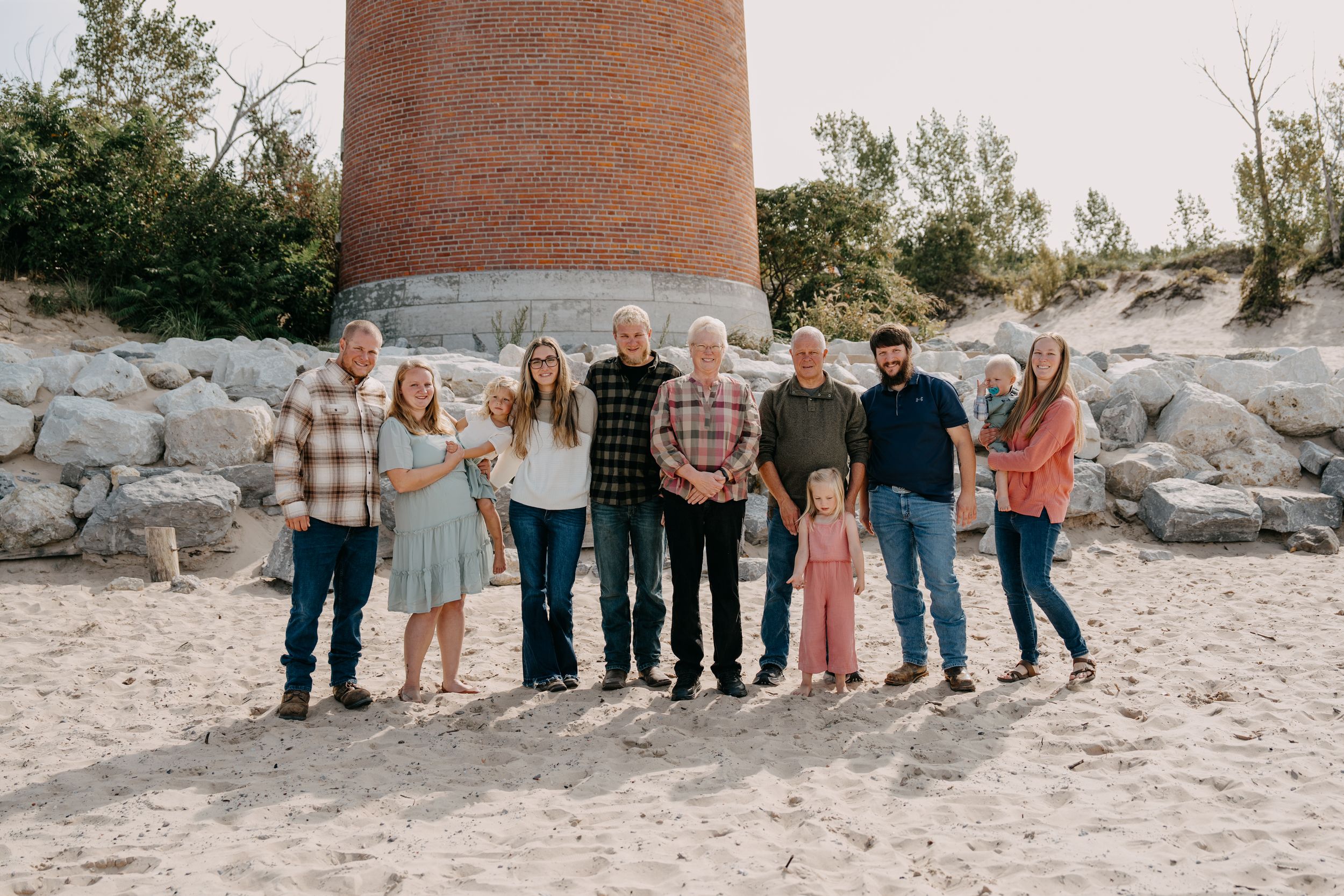 Family group standing together on a beach near large brick lighthouse tower during sunset.