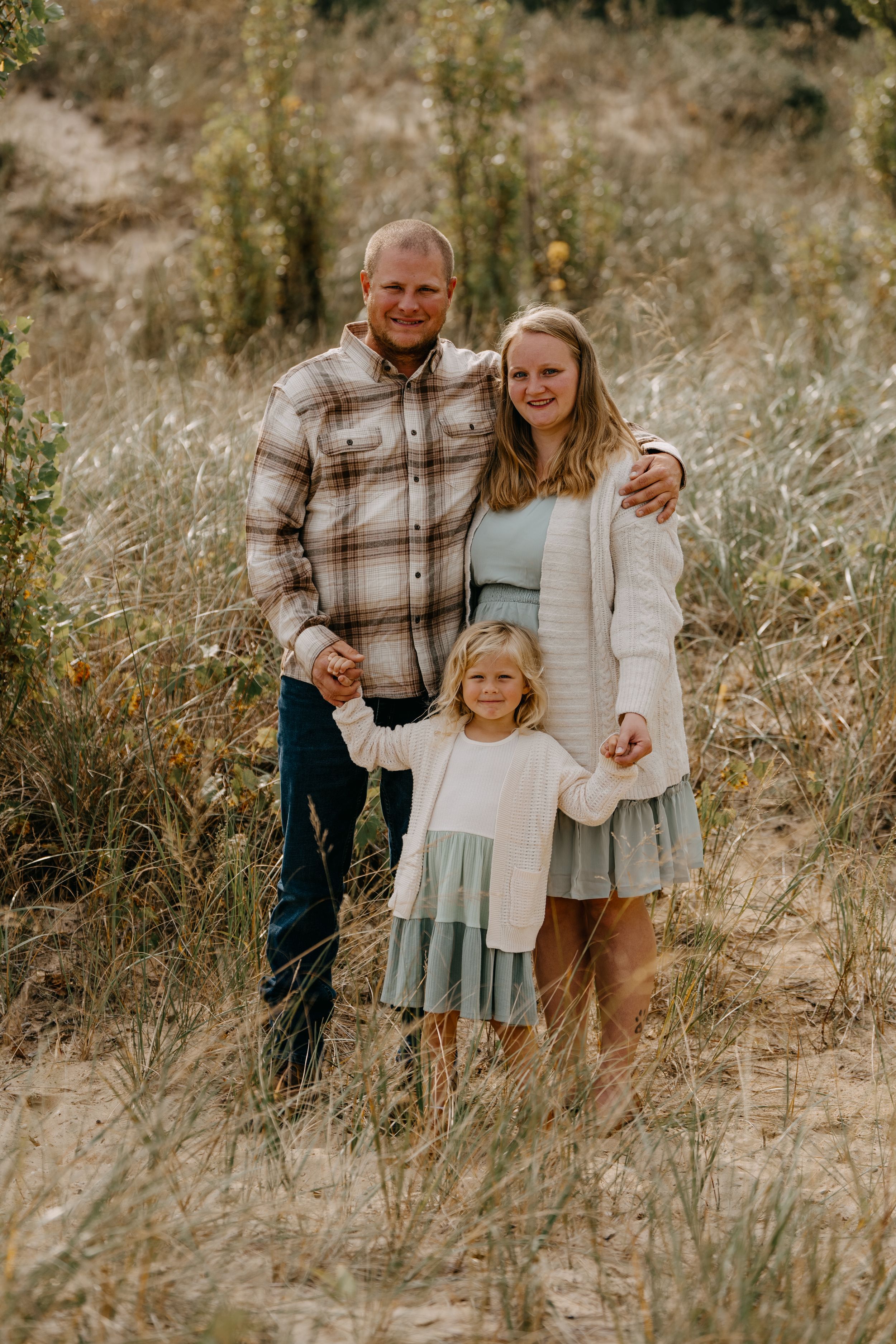 A family in coordinated neutral tones poses together in a grassy field during golden hour.