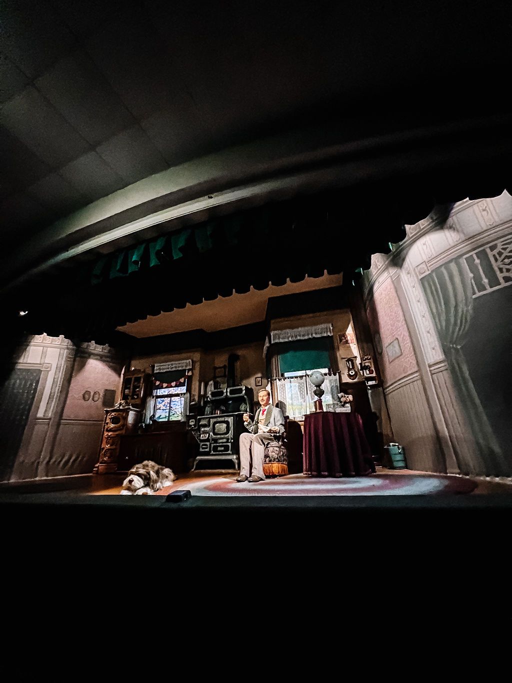 Dark theater stage with dramatic lighting illuminates art deco-style architectural elements and props.