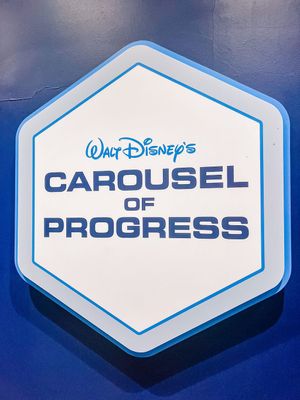 White hexagonal Disney signs reading 'Carousel of Progress' displayed on a dark blue backdrop.
