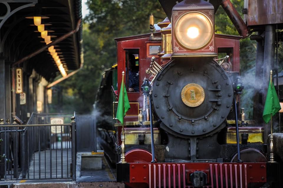 Vintage steam locomotive engine with glowing headlight approaches along train tracks at twilight.