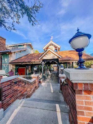 Looking down a concrete walkway with brick walls and blue decorative finials leading to a beach-style building entrance.
