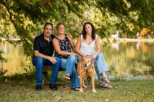 Group relaxing together with their dog by a serene lake during golden hour in a park setting.