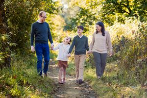 A family walks together through a sunlit autumn path surrounded by golden foliage and natural scenery.