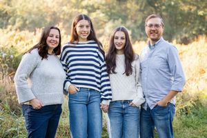 A family of four wearing coordinated blue and white outfits poses together outdoors in golden sunlight.