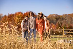 A group of people stand together in a golden autumn field with colorful fall foliage in the background.