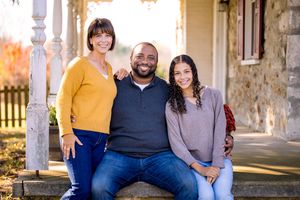 Family portrait session with couple and child sitting together on stone steps in outdoor courtyard setting.