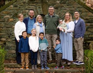 A group of people stand together in front of a rustic stone wall during an outdoor photo session.