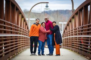 A family walks together across a rustic wooden bridge on an autumn day.