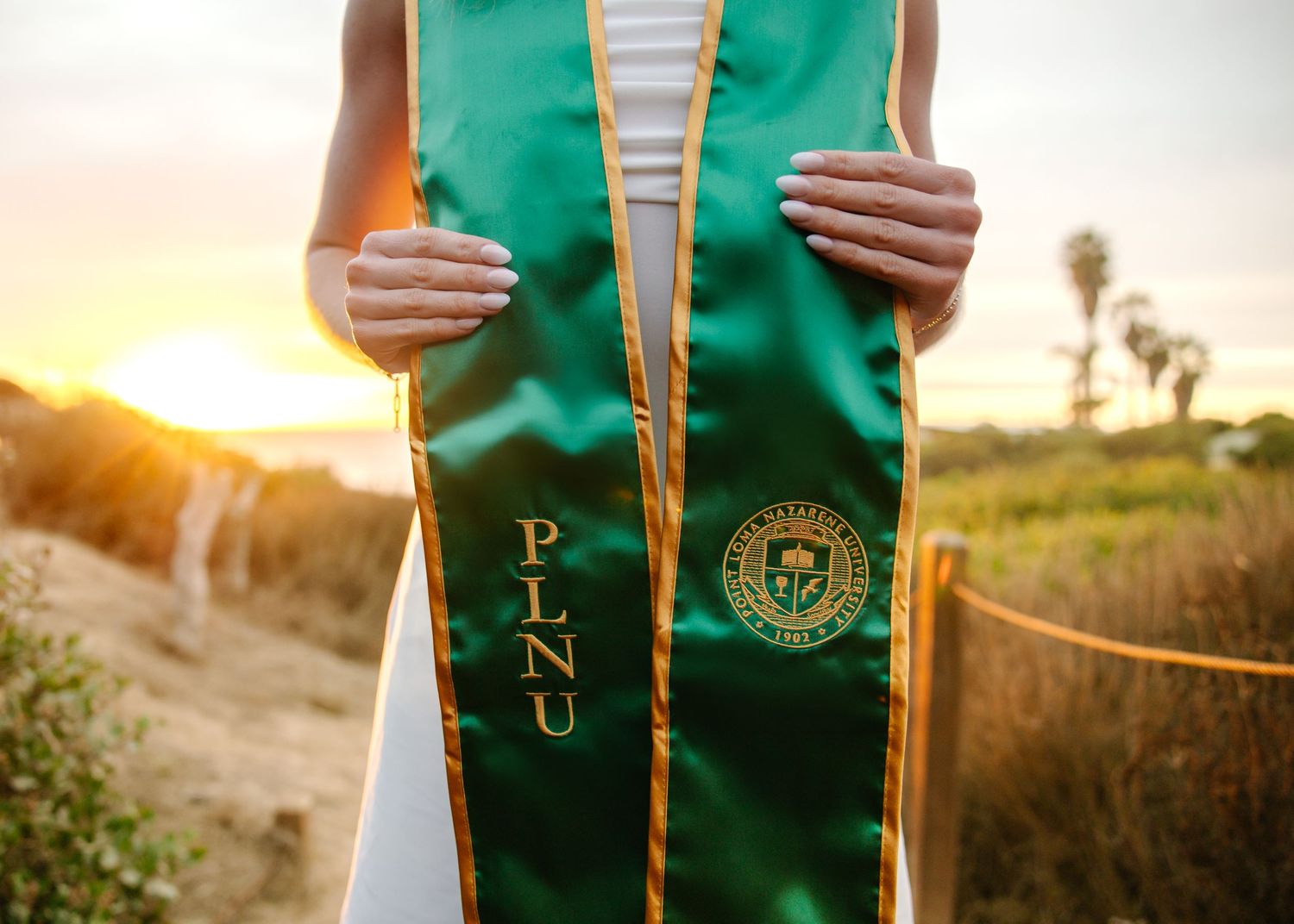 Graduate in emerald green stole poses in front of white columns during graduation photos.