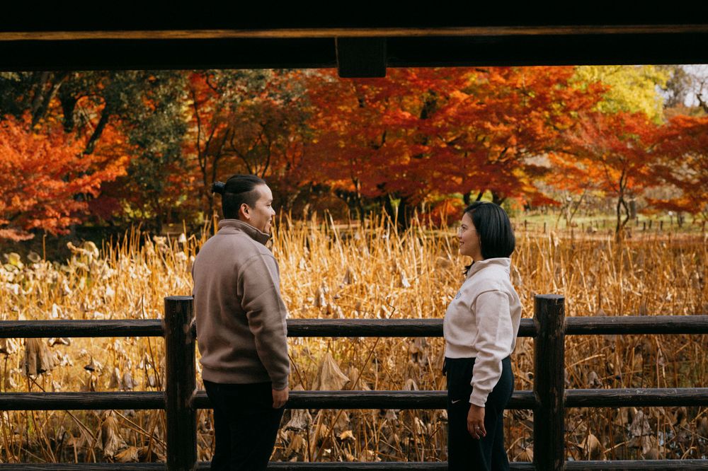 Couple facing each other on a bridge surrounded by stunning red and orange autumn fall foliage.