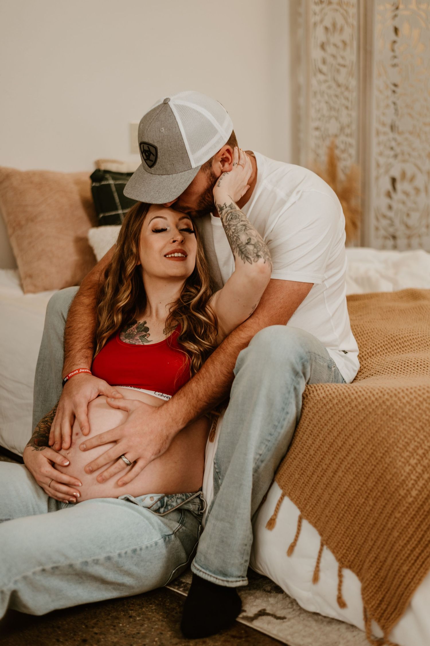 An intimate maternity photo of a couple relaxing on a couch in casual attire.