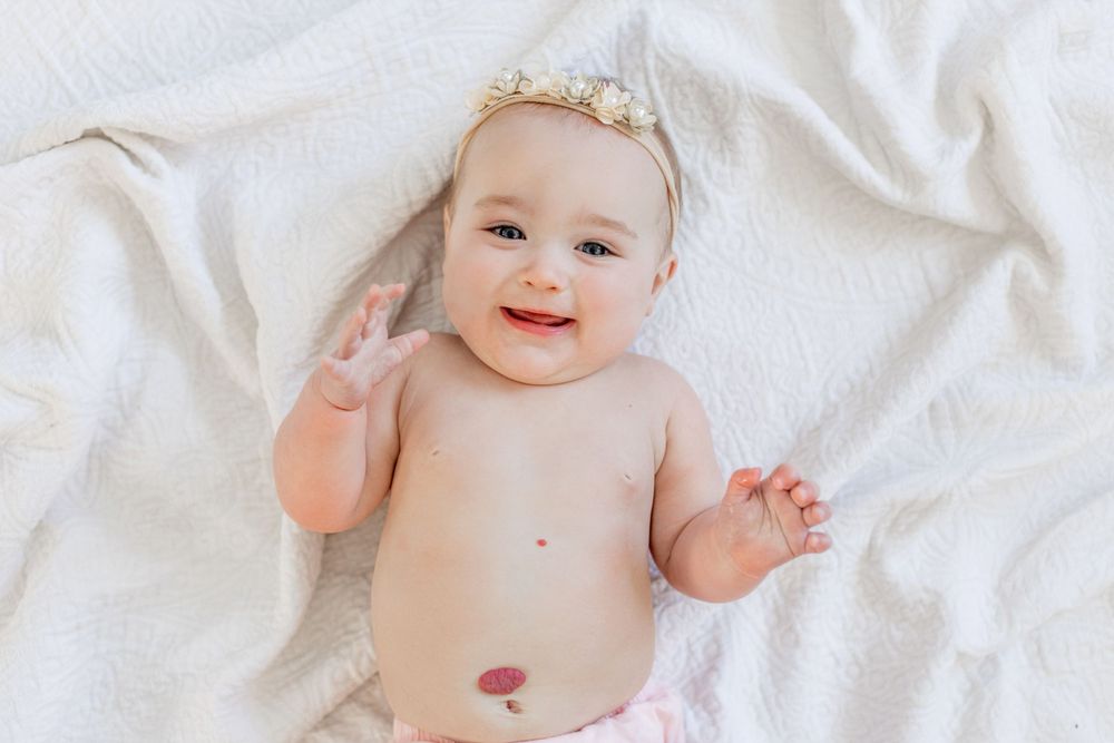 Happy baby wearing a delicate floral headband lies on white blanket in Springfield, Missouri.