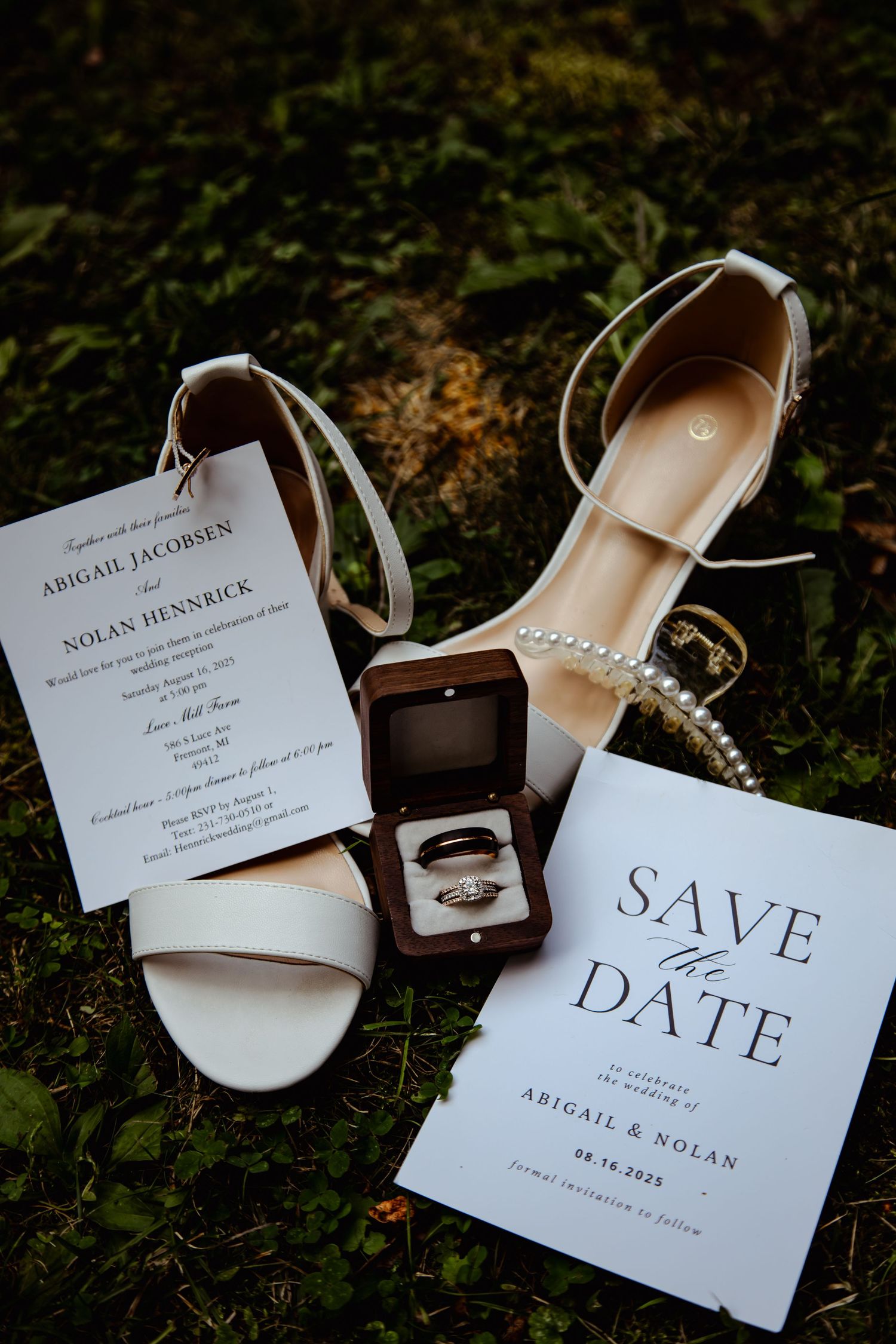 Wedding invitation cards and elegant bridal accessories arranged on dark mossy ground in a creative flat lay composition.
