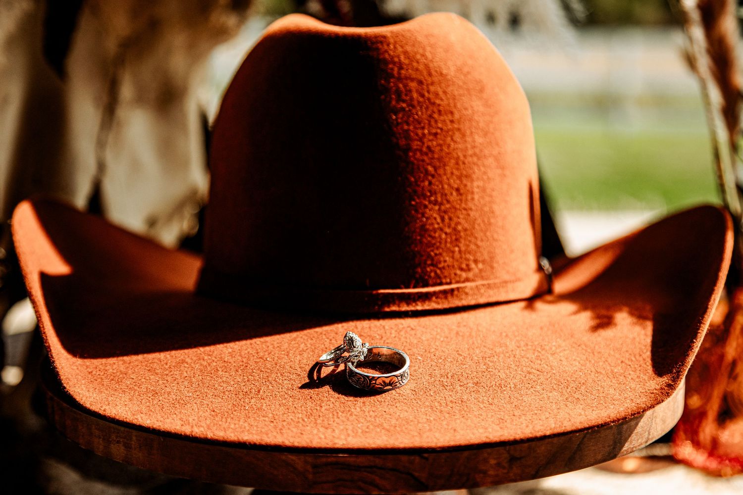 A brown leather cowboy hat with decorative details sits on a wooden surface in warm lighting.