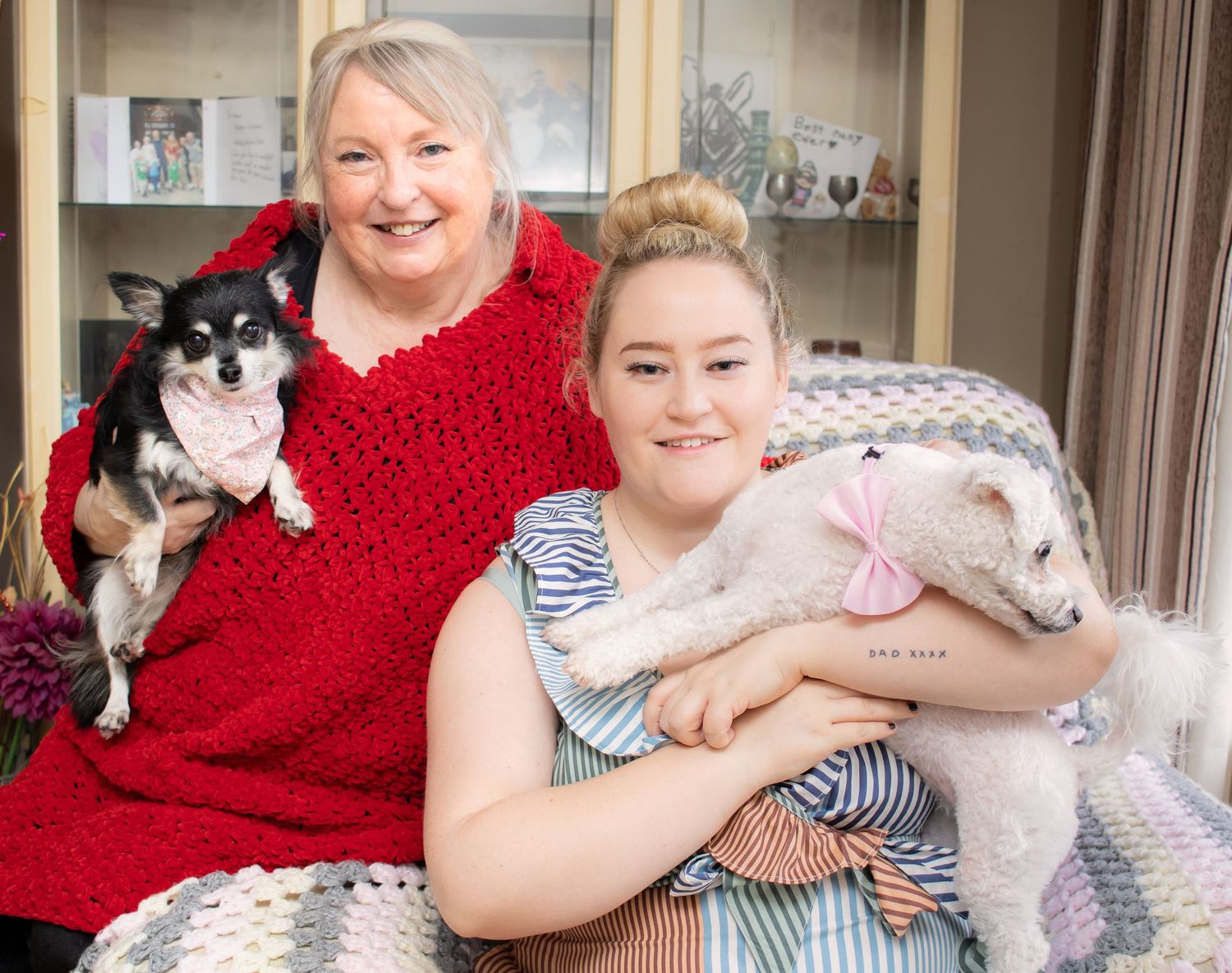 A cozy family photo showing two people on a couch with their chihuahua and white dog.