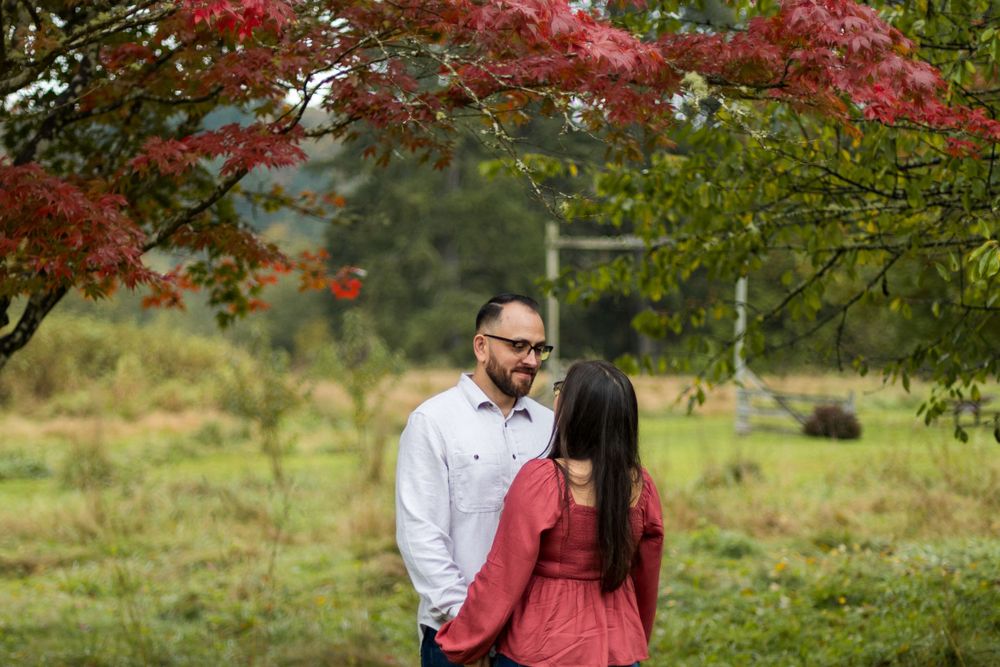 A couple stands under vibrant red maple leaves in a peaceful garden setting during autumn.