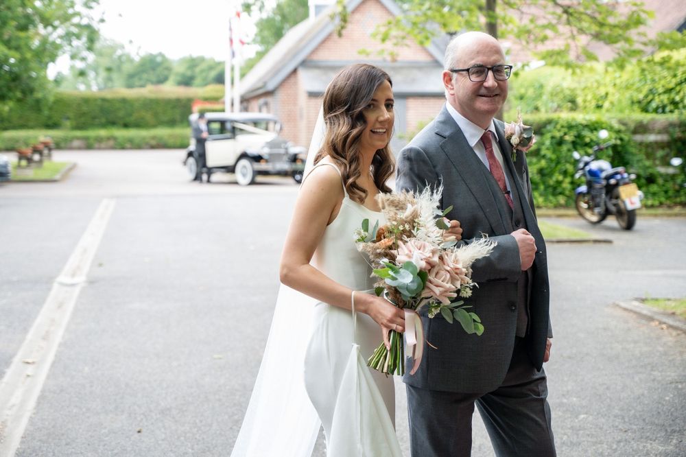Person carries bouquet while walking along outdoor pathway near parked vehicles.