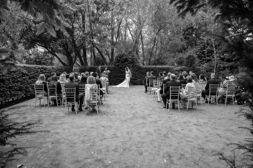 Black and white photo of outdoor wedding ceremony with guests seated in rows among trees.