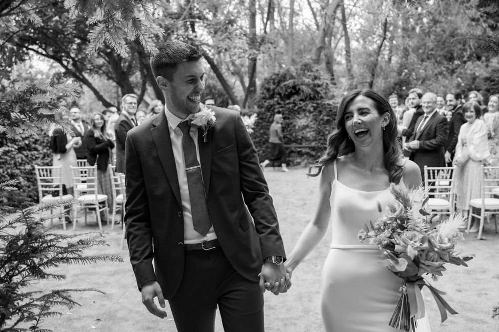 Couple walking together during outdoor garden wedding ceremony among seated guests.