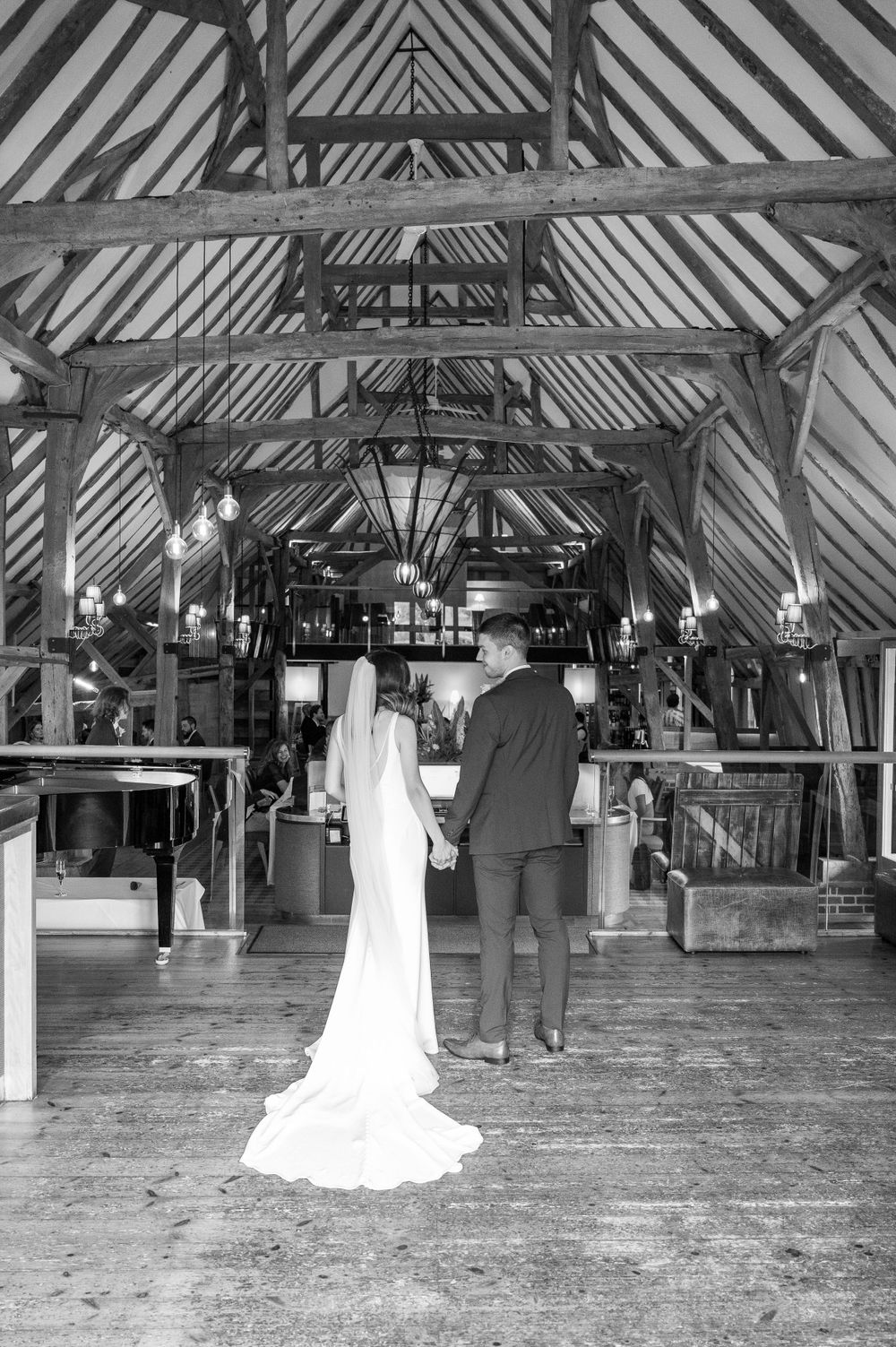 A couple stands in a rustic barn venue with exposed wooden beams and dramatic lighting.