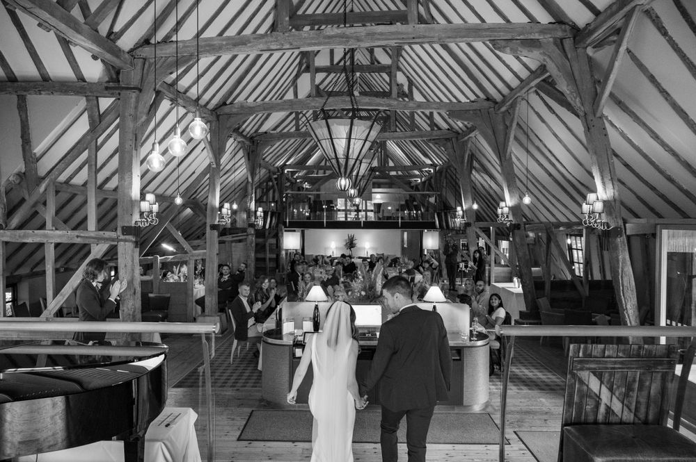 Black and white photo of a wedding ceremony in a historic timber-framed barn with vaulted ceilings.