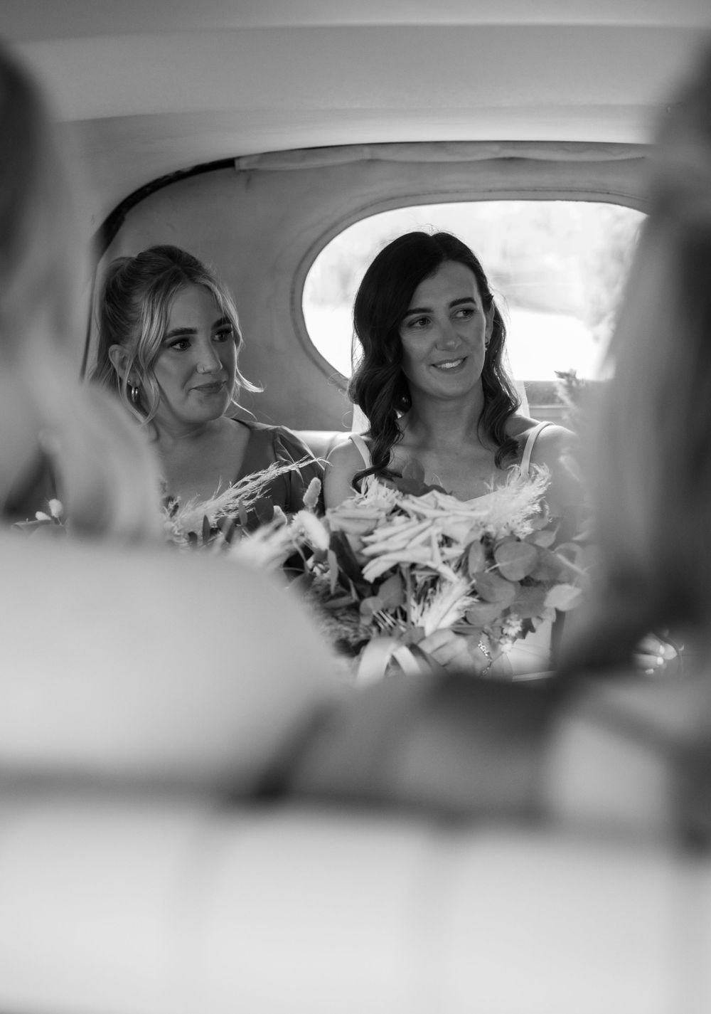 Two elegantly dressed attendants share a moment in the backseat of a car.