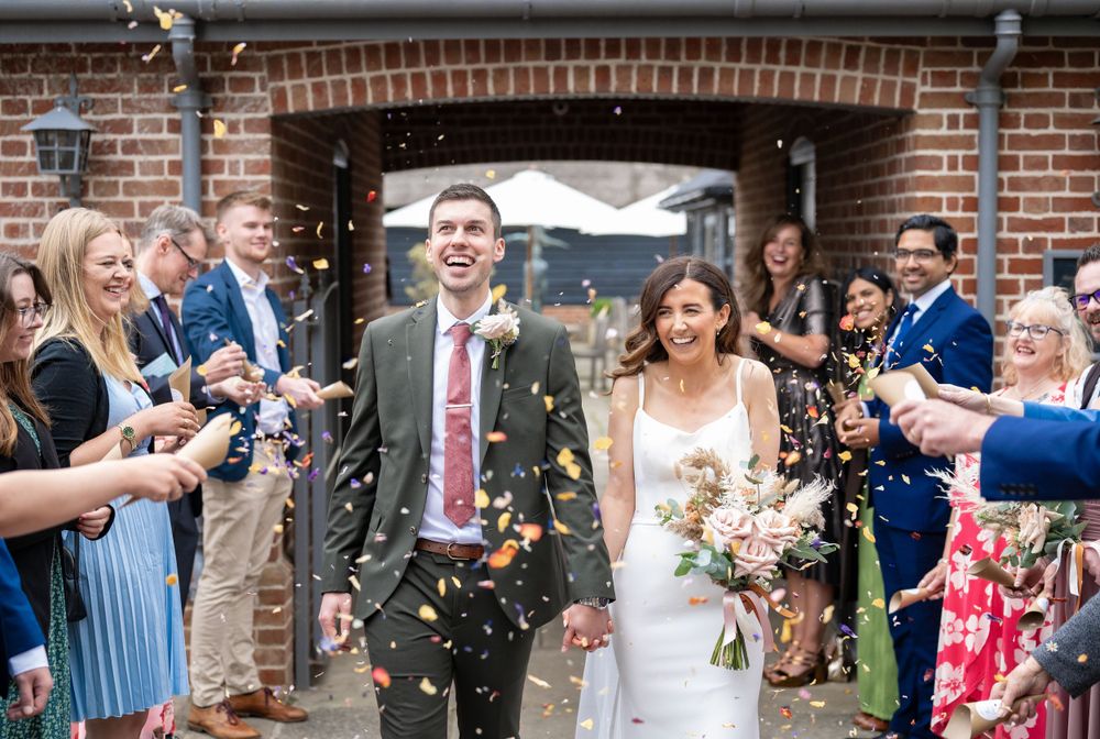 Wedding guests shower the newlyweds with confetti as they exit through a brick archway.