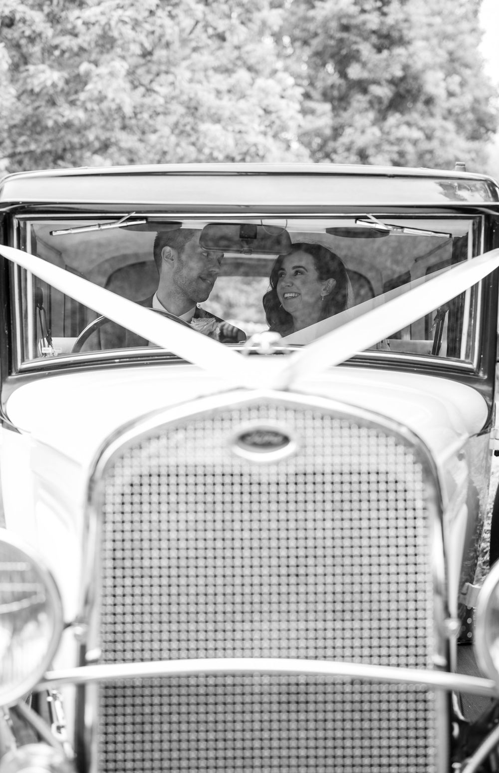 A classic vintage car frames the happy couple through its windshield in black and white.