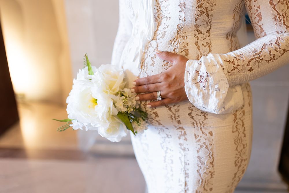 Bride in white lace gown holding elegant white floral bouquet, showcasing diamond ring on her hand.