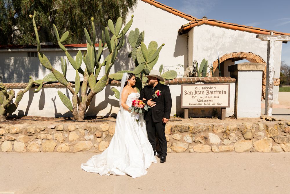 Bride and groom pose outside historic Mission San Juan Bautista with cactus backdrop on their wedding day.