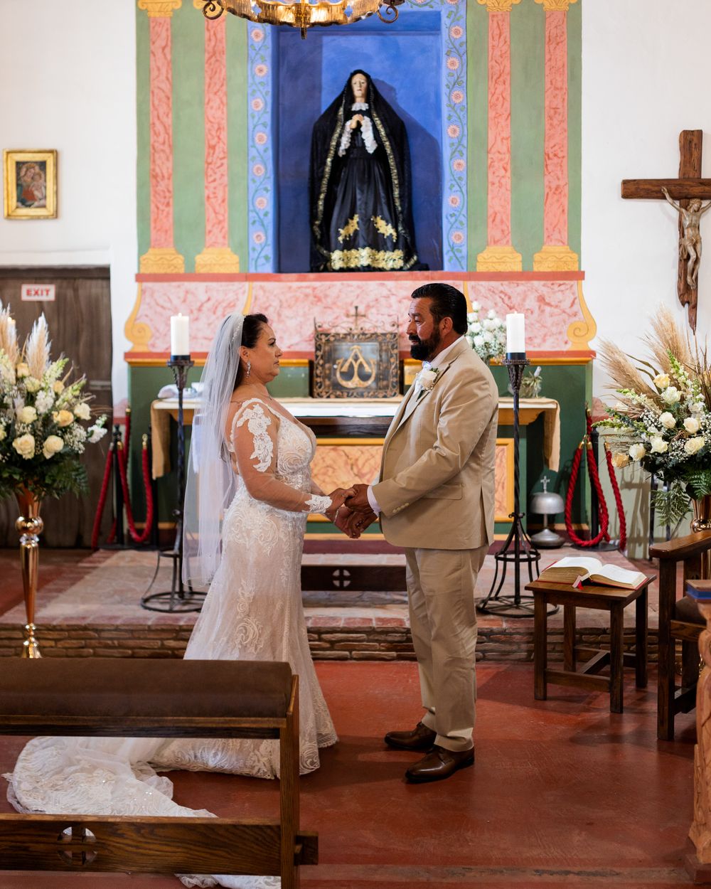 A wedding ceremony taking place in a traditional Catholic church with colorful painted walls and religious statues.